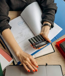 A business professional uses a calculator among documents and laptop on a desk for financial tasks.